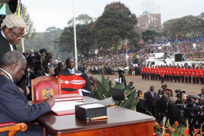 President Mwai Kibaki signs the new constitution into law at a public function witnessed by the Nation at Uhuru Park, Nairobi. Standing by is Attorney General Amos Wako.