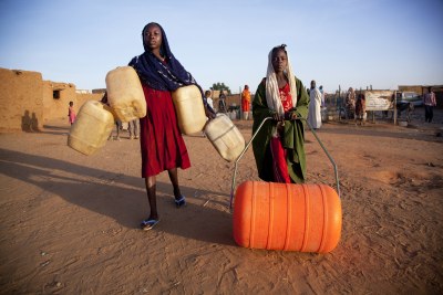 A child pushes an orange Water Roller, which has the same capacity as the four jerry cans carried by her companion.