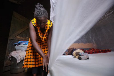A mother secures her child under a mosquito net.